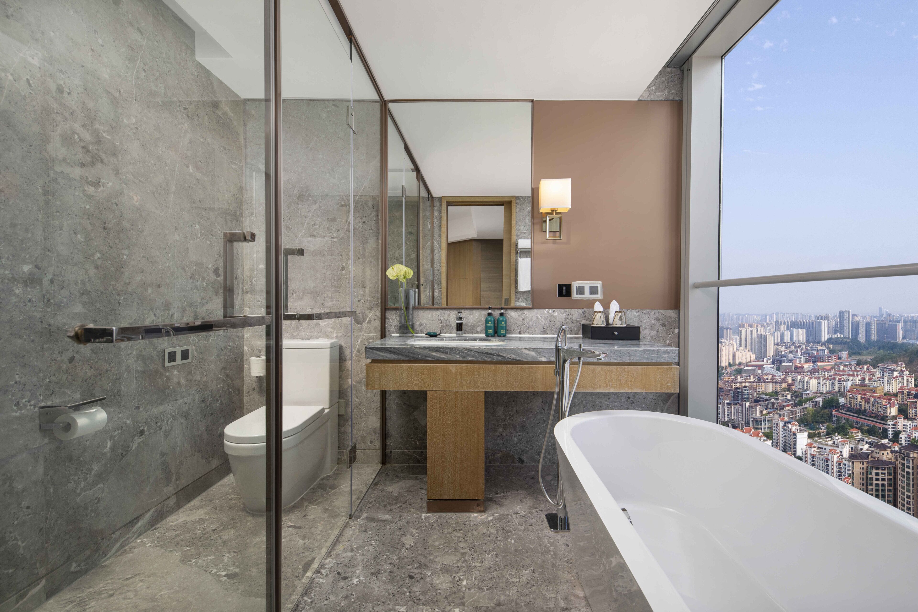 Une salle de bain moderne dotée d’une douche à parois de verre, de toilettes, d’un lavabo avec miroir et d’une baignoire offrant une vue sur la ville.