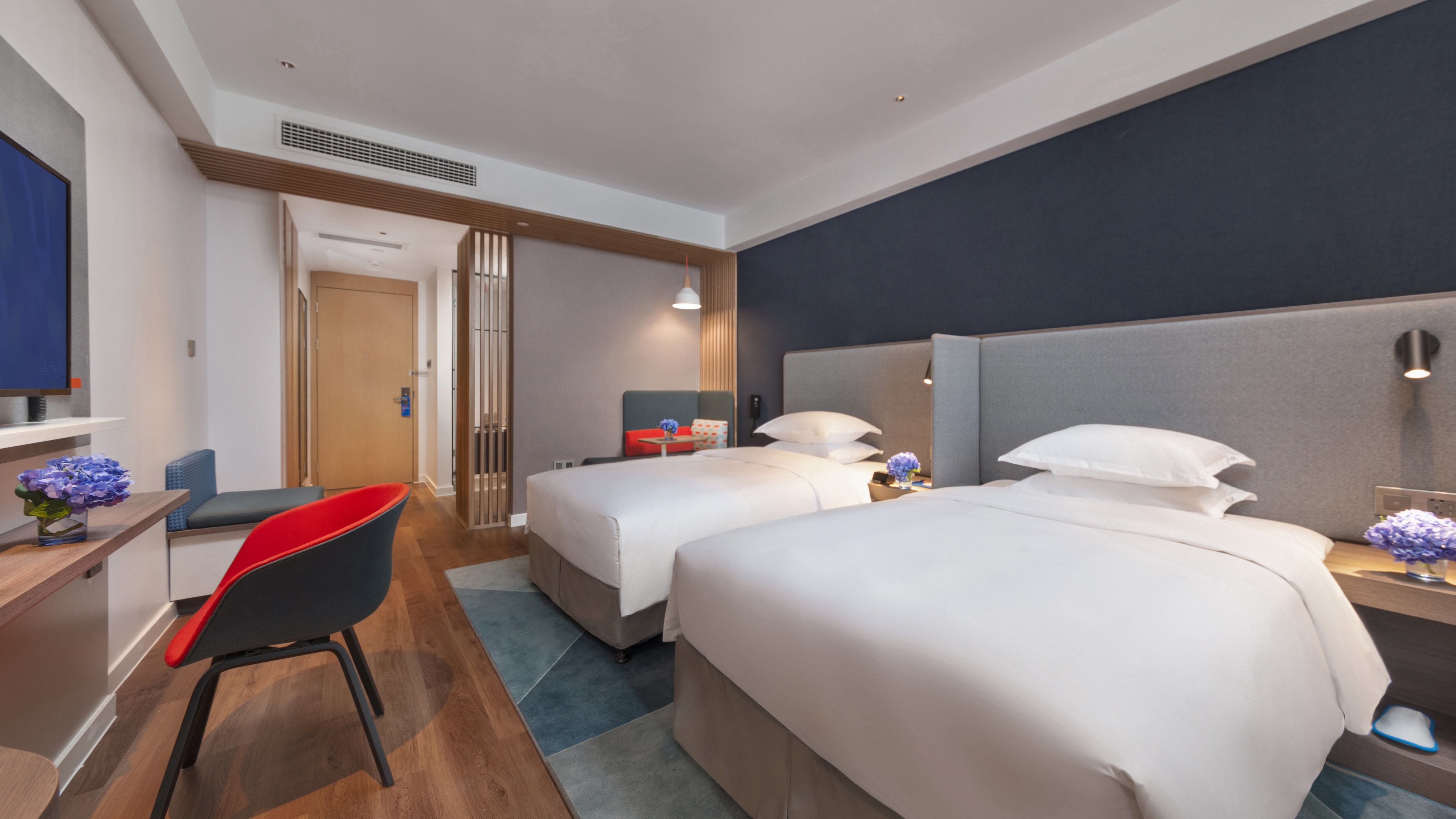 A hotel room with two beds, a desk, a chair, and a TV.