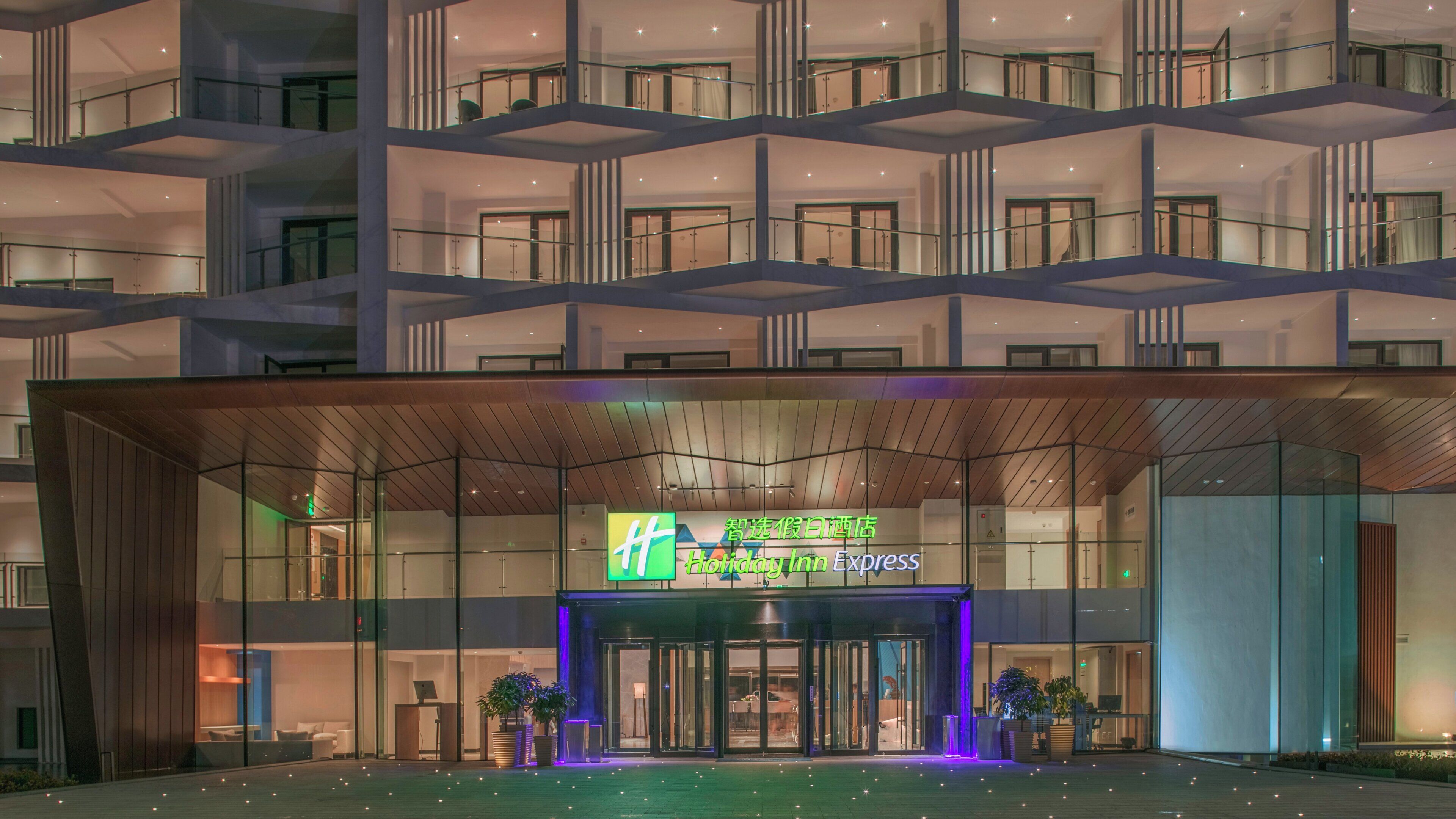 Ein modernes Hotel mit Glasfassade, einem markanten Eingang mit einer blau beleuchteten Drehtür und einem Schild mit 'Holiday Inn Express'.