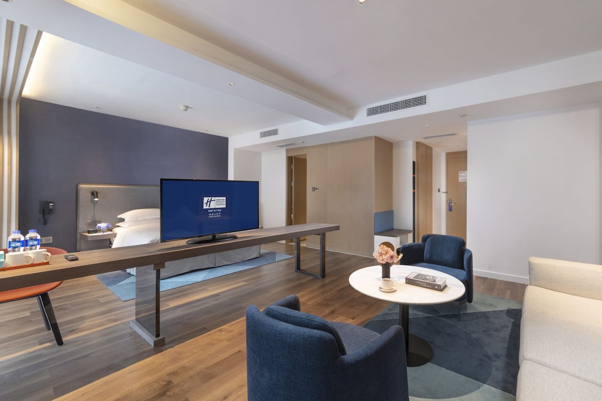 A modern hotel room with a flat-screen TV, a sofa, a chair, a coffee table, and a desk.