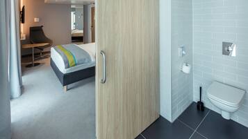 Una habitación de hotel moderna con una cama, un escritorio y un baño con inodoro y lavabo.