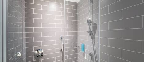 A shower with a glass door, grey tiled walls, and a handheld showerhead.