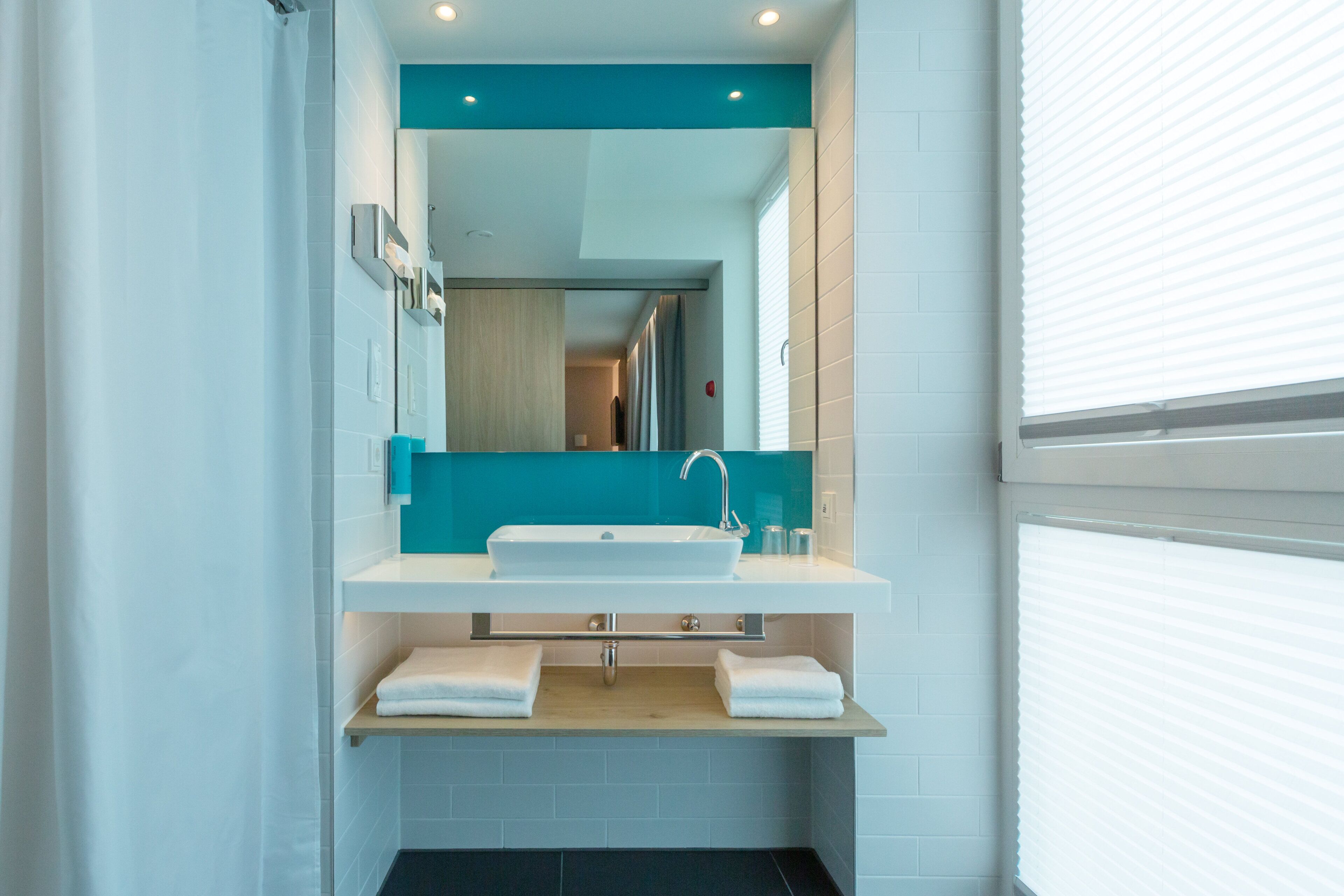 A modern bathroom with a white sink, teal accent wall, and a mirror above it.