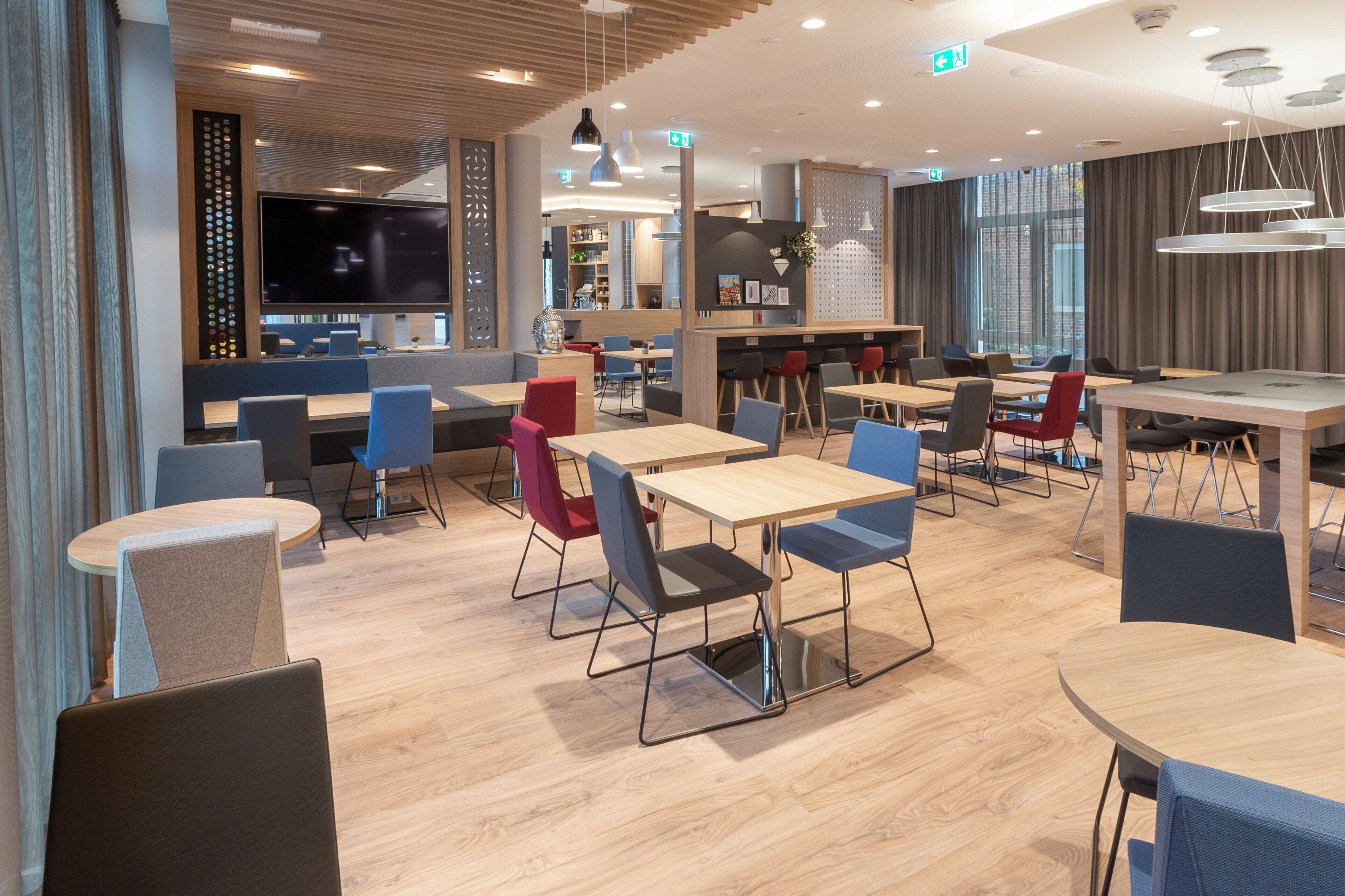 A modern dining area with multiple tables and chairs, a large flat-screen TV, and a bar area with shelves and decorative items.