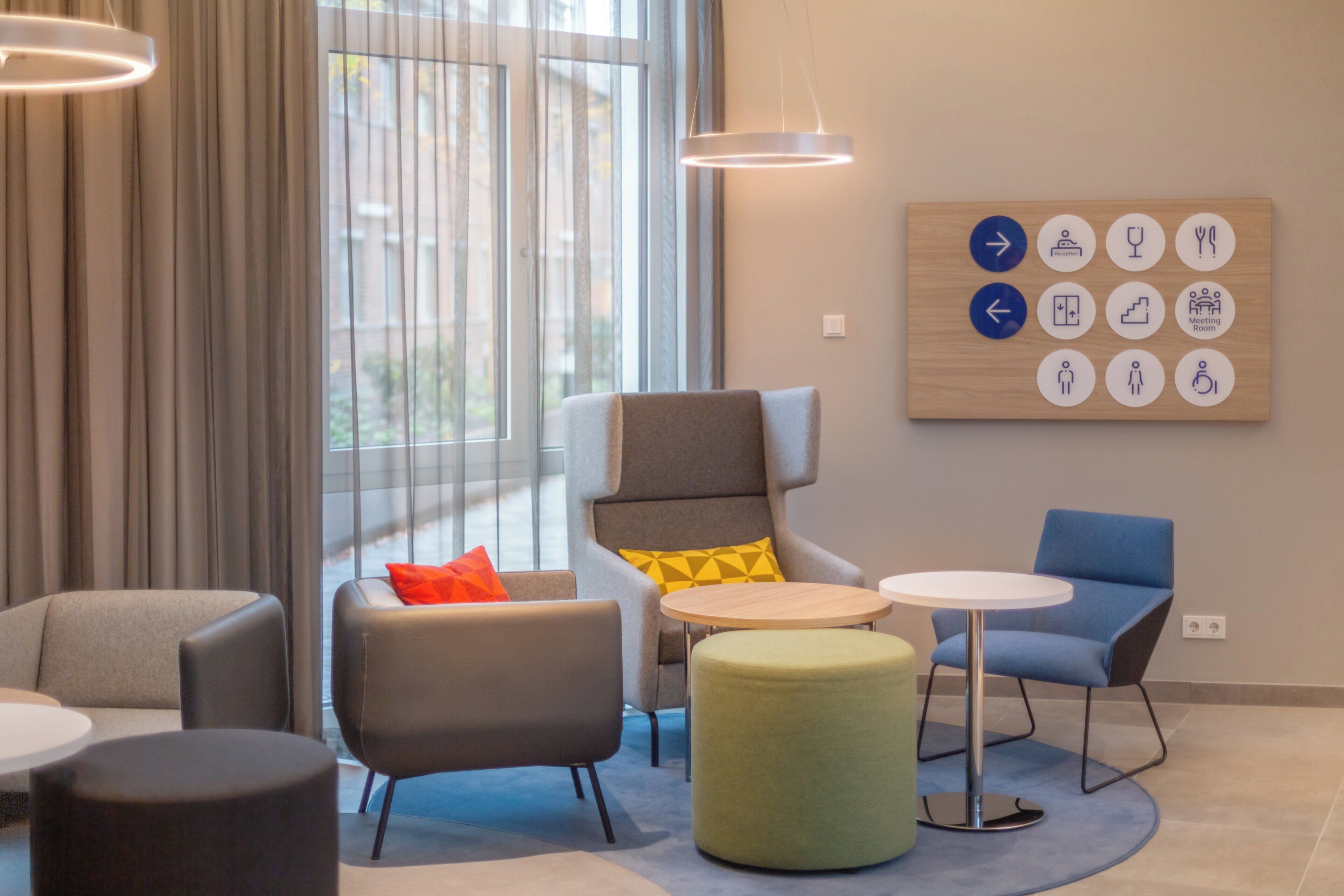 Ett modernt loungeområde med sittplatser, en receptionsskylt och vägvisningssymboler.