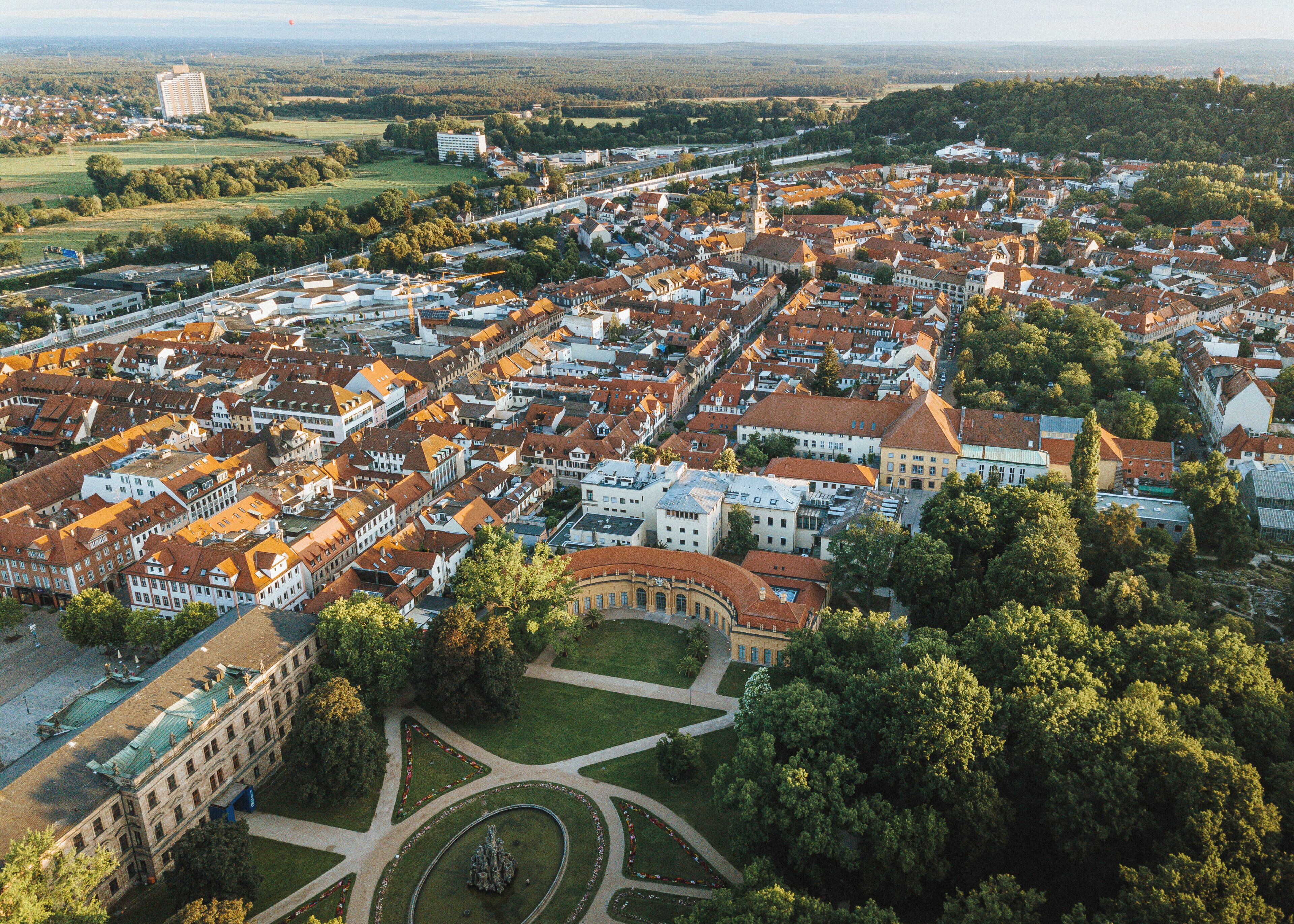 Eine Luftaufnahme einer Stadt mit historischen Gebäuden, einem zentralen Kreisverkehr und umgebender Natur.