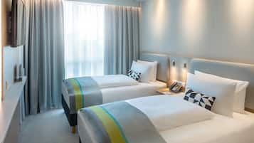 A hotel room with two beds, a desk, a telephone, and a window with curtains.