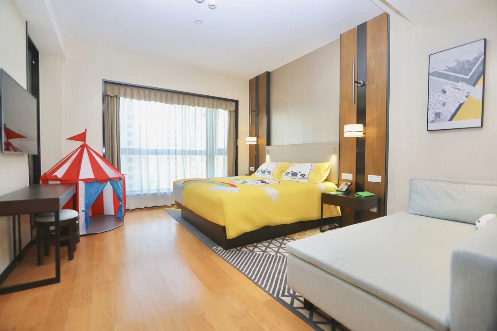 Habitación de hotel con cama, escritorio, silla, mesita, sofá y ventana con cortinas.