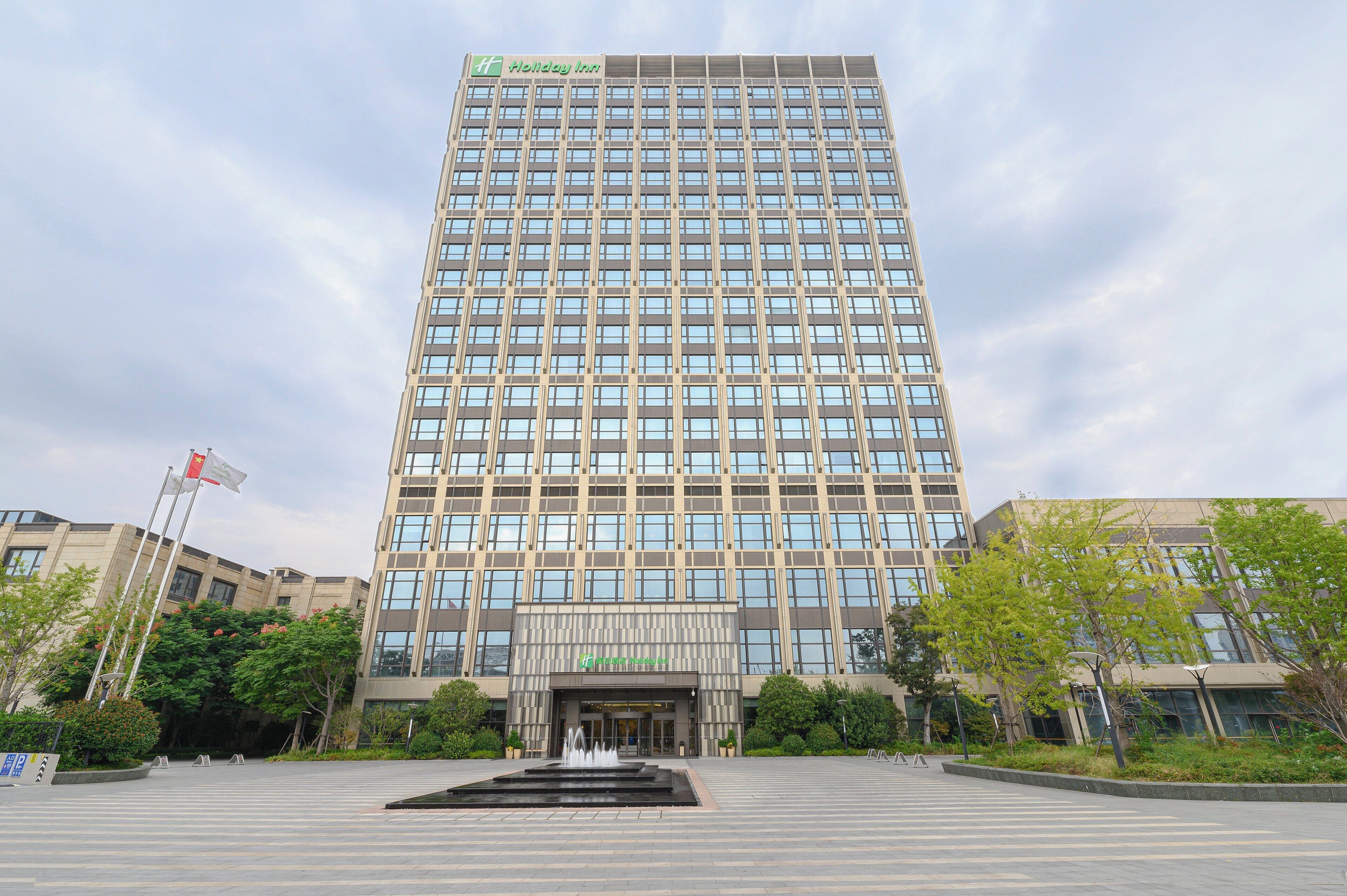 Un edificio alto y moderno con un letrero de Holiday Inn, que presenta una entrada amplia con una fuente ornamental al frente.