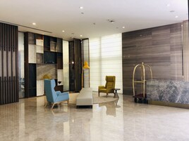 Un vestíbulo moderno con un sillón azul, un sillón amarillo, un reposapiés blanco, una lámpara dorada y un mostrador de recepción de mármol.