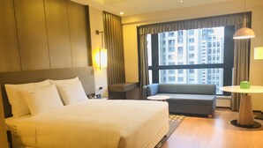 Camera d'albergo con un letto grande, un divano, un tavolo e vista sulla città dalla finestra.