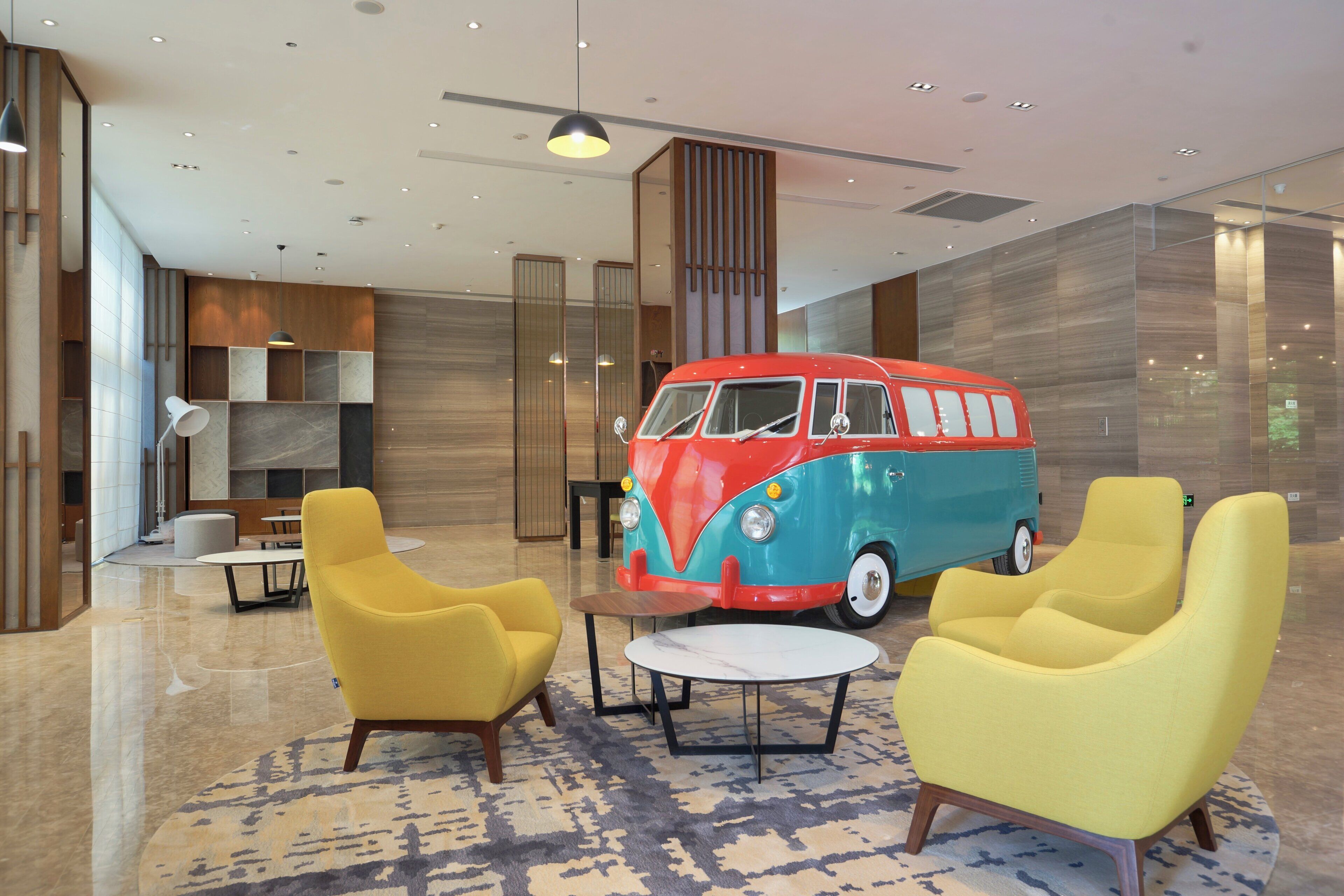 A modern lobby with yellow armchairs, a red and blue van, and a marble-patterned carpet.