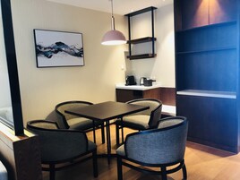 A modern dining area with a table and four chairs, a pendant light, a coffee machine, and a framed artwork on the wall.