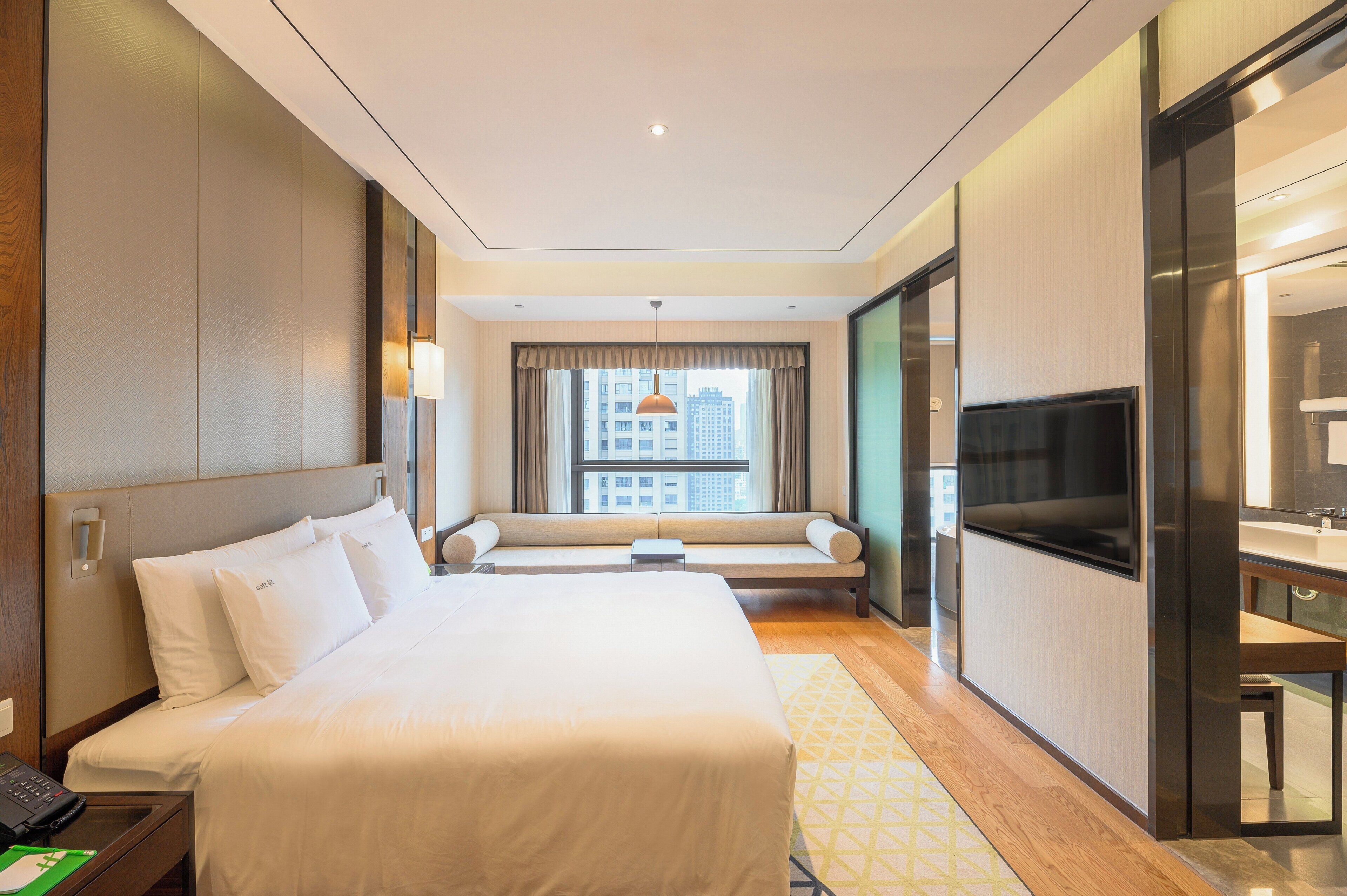 A hotel room with a large bed, a sofa, a television, and a bathroom.