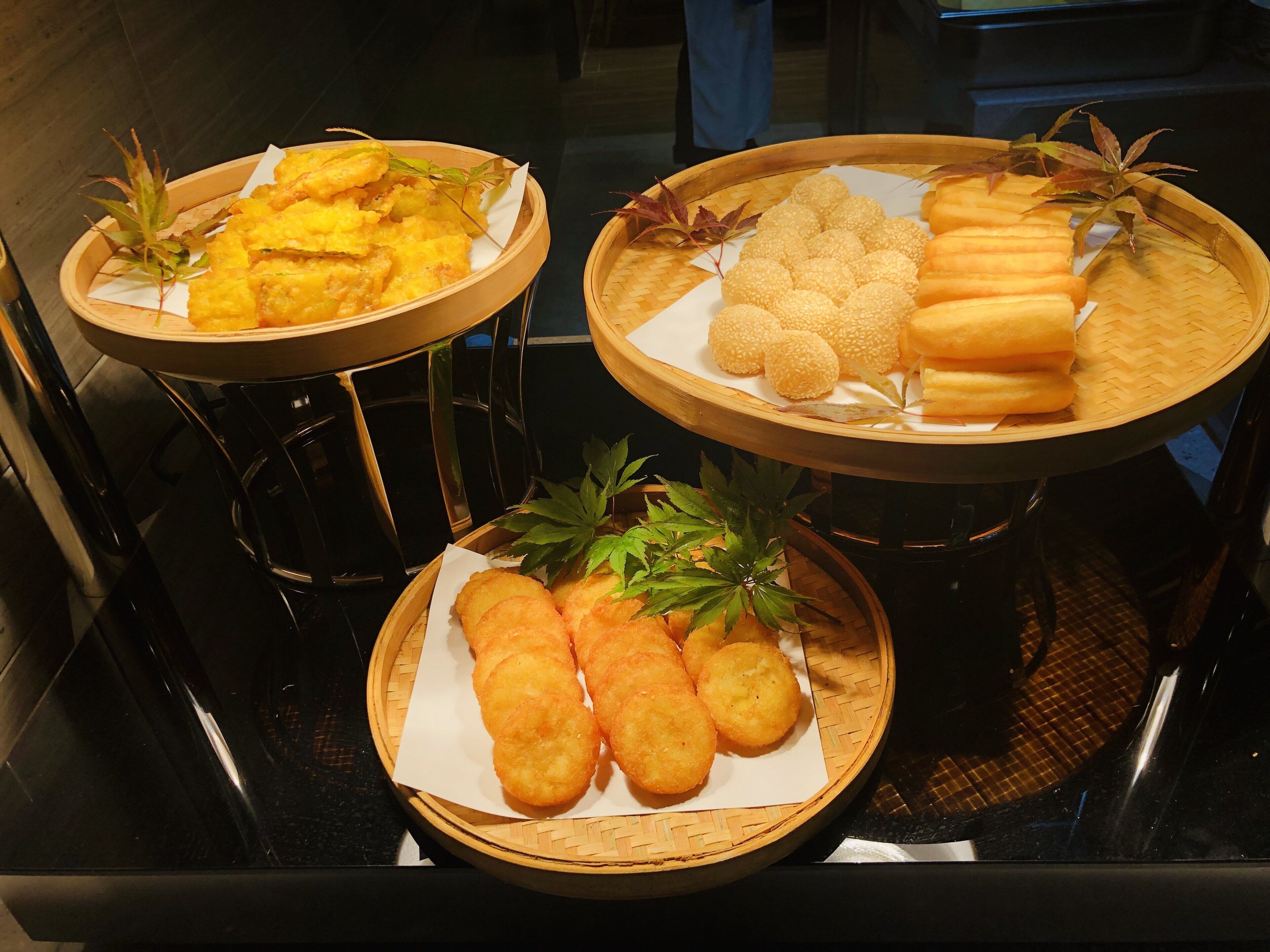 Three wooden trays with various fried foods on a black countertop.