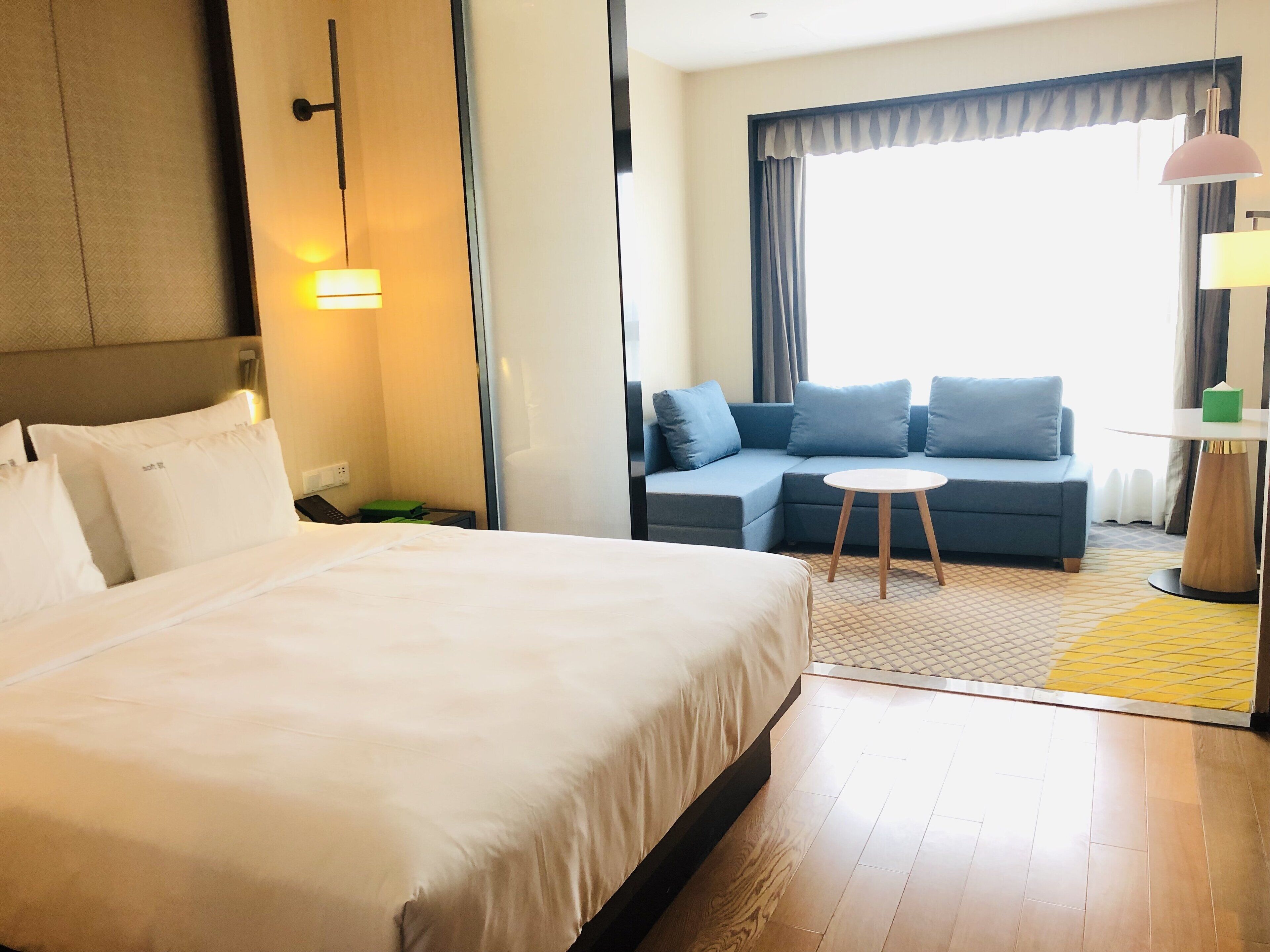 A hotel room with a large bed, a sofa, a small table, and a window with curtains.