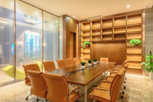 A conference room with a long table, multiple chairs, and wooden shelving with plants.