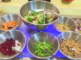 Una mesa de buffet con diversos alimentos, entre ellos zanahorias, remolachas, judías verdes y garbanzos.