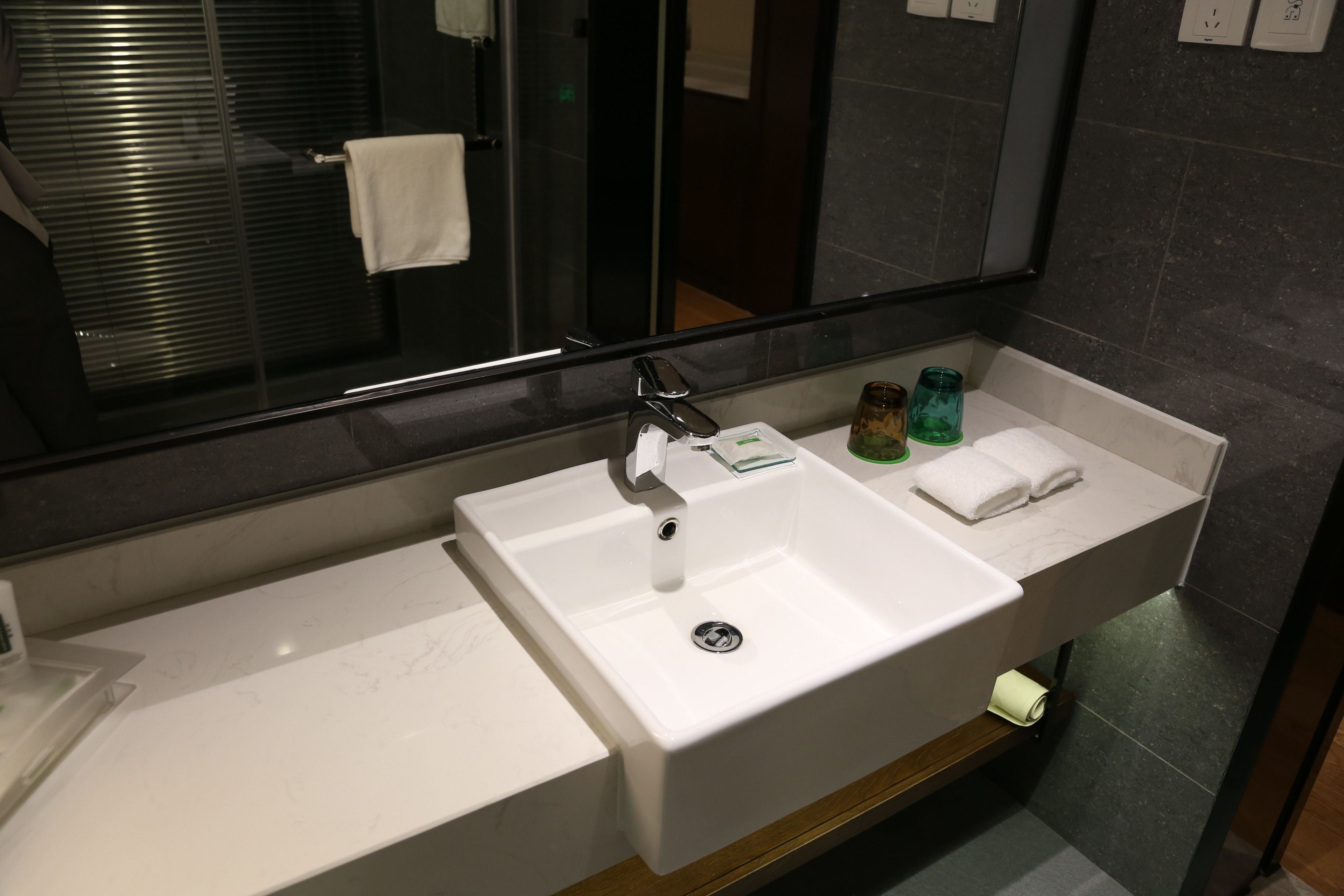 Ein modernes Badezimmer mit einem großen Spiegel, einem weißen Waschbecken und einer Duschkabine aus Glas.
