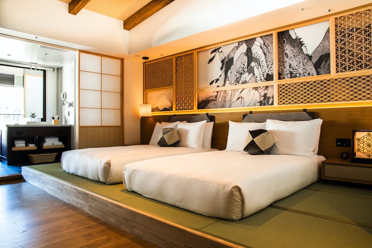 A hotel room with two beds, a wooden headboard, a tatami mat floor, and a traditional Japanese sliding door.