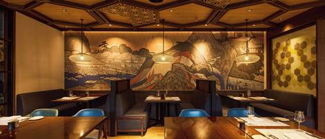 A restaurant with wooden tables and chairs, a mural on the wall, and hanging pendant lights.
