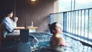 Un entorno de spa con un jacuzzi y una mesa con una botella, una persona sentada en el jacuzzi y otra persona en la mesa.