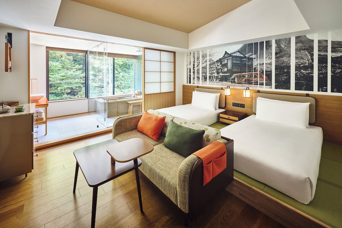 A hotel room with a bed, a sofa, a small table, a desk, and a window with a view of greenery.
