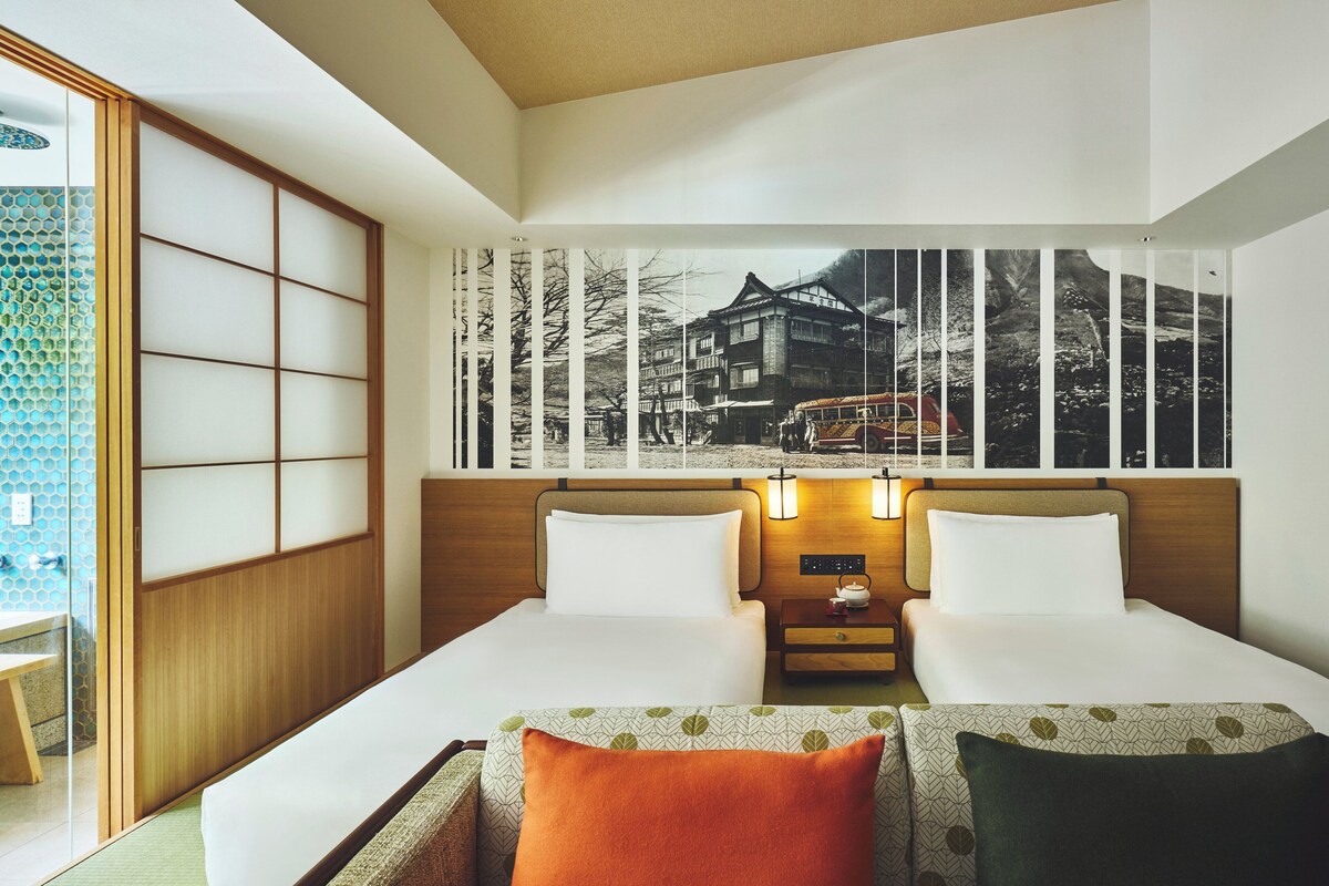Una habitación de hotel con cama, dos mesitas de noche, un televisor montado en la pared y un panel corredero estilo shoji.