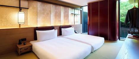 Habitación de hotel con dos camas, una mesita de noche de madera, un muro al estilo tradicional japonés y vista a la vegetación a través de un puertas correderas.