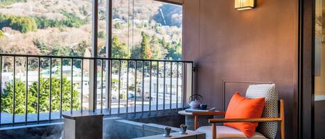 A balcony with a view of a mountainous landscape, a seating area with a chair and a table, and a wall-mounted light fixture.
