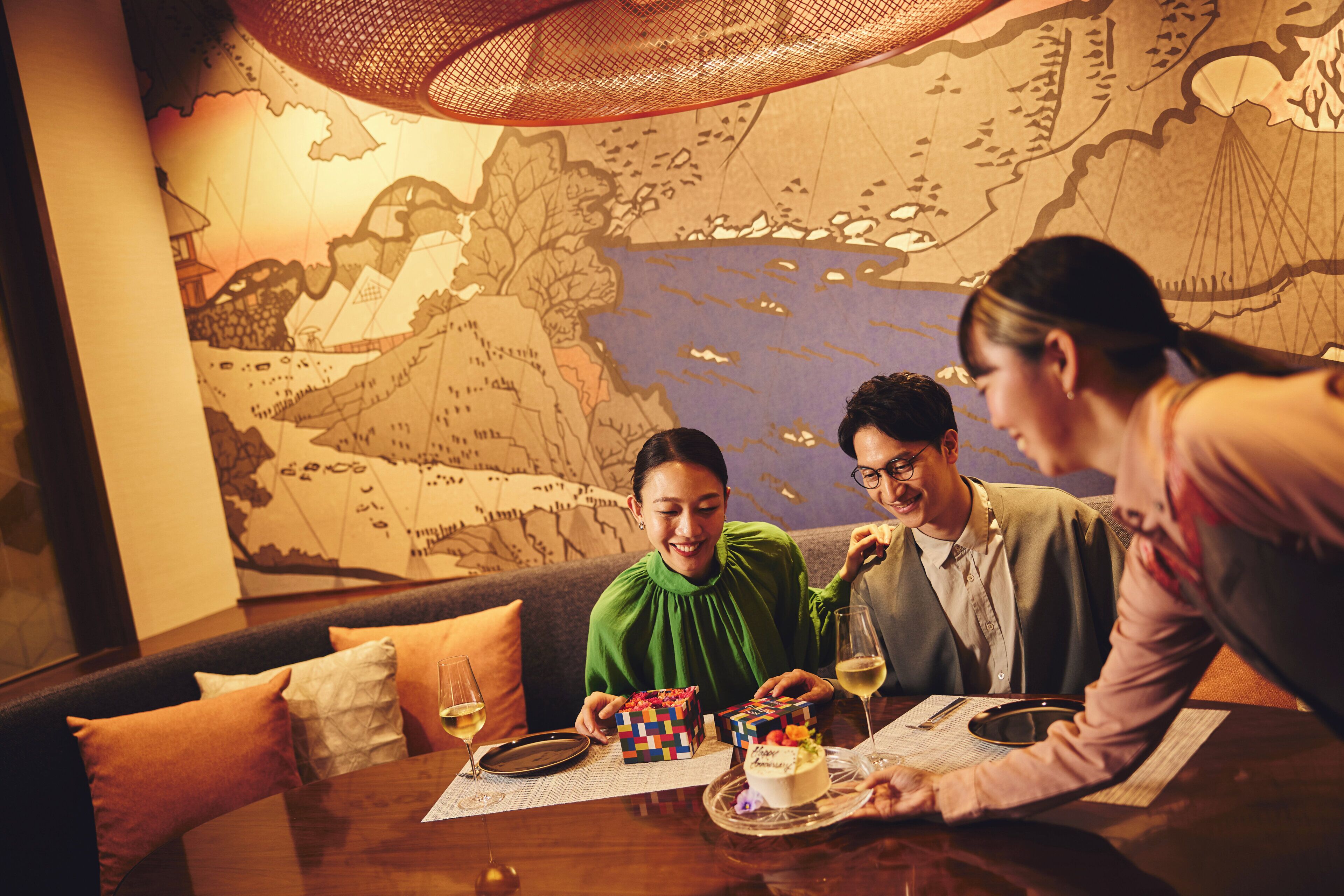 A group of people seated at a table with a world map mural in the background.
