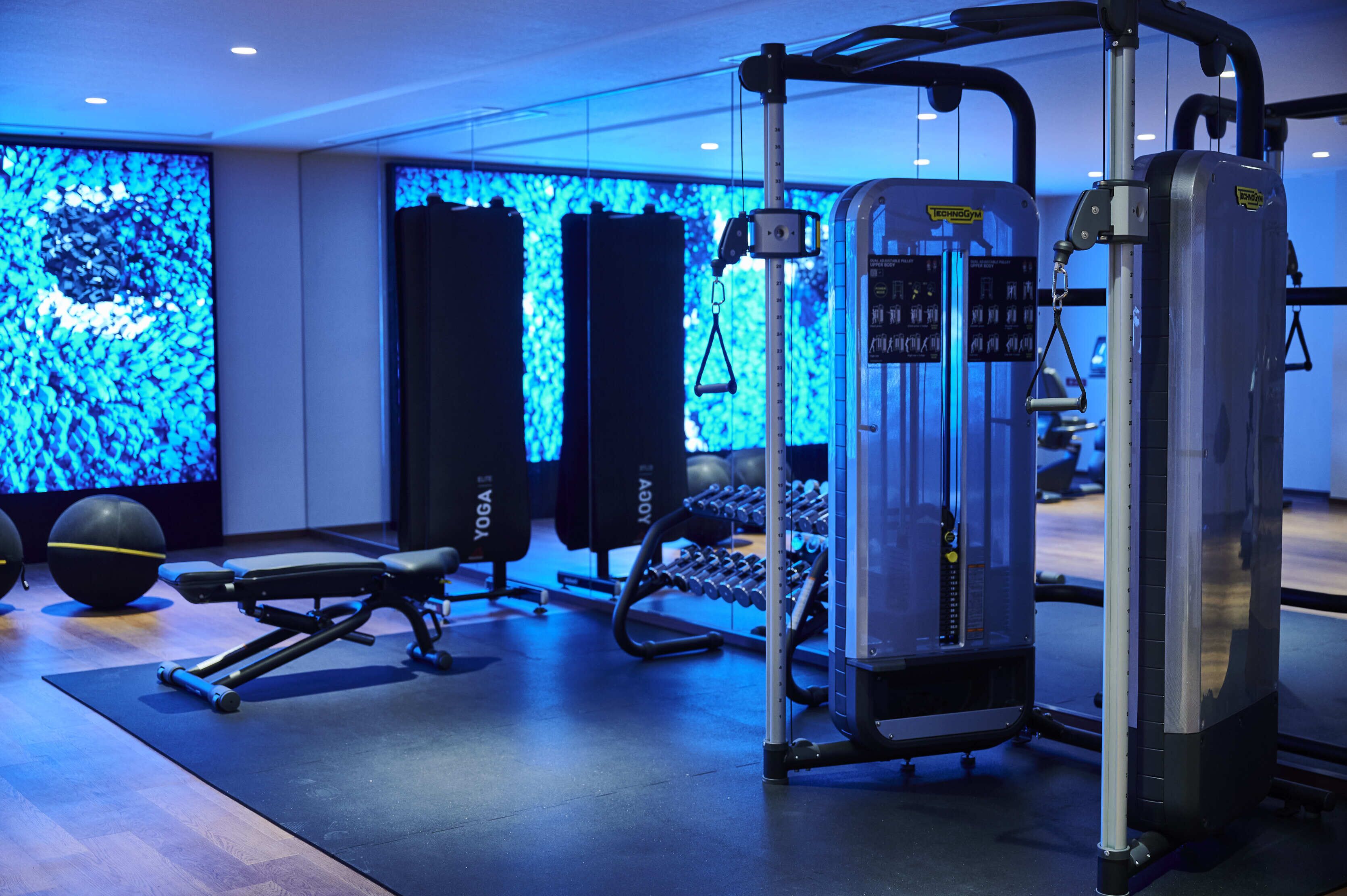 Un gimnasio con equipamiento de ejercicio, una banca y una pared con una iluminación azul.