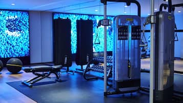 Un gimnasio con equipamiento de ejercicio, una banca y una pared con una iluminación azul.
