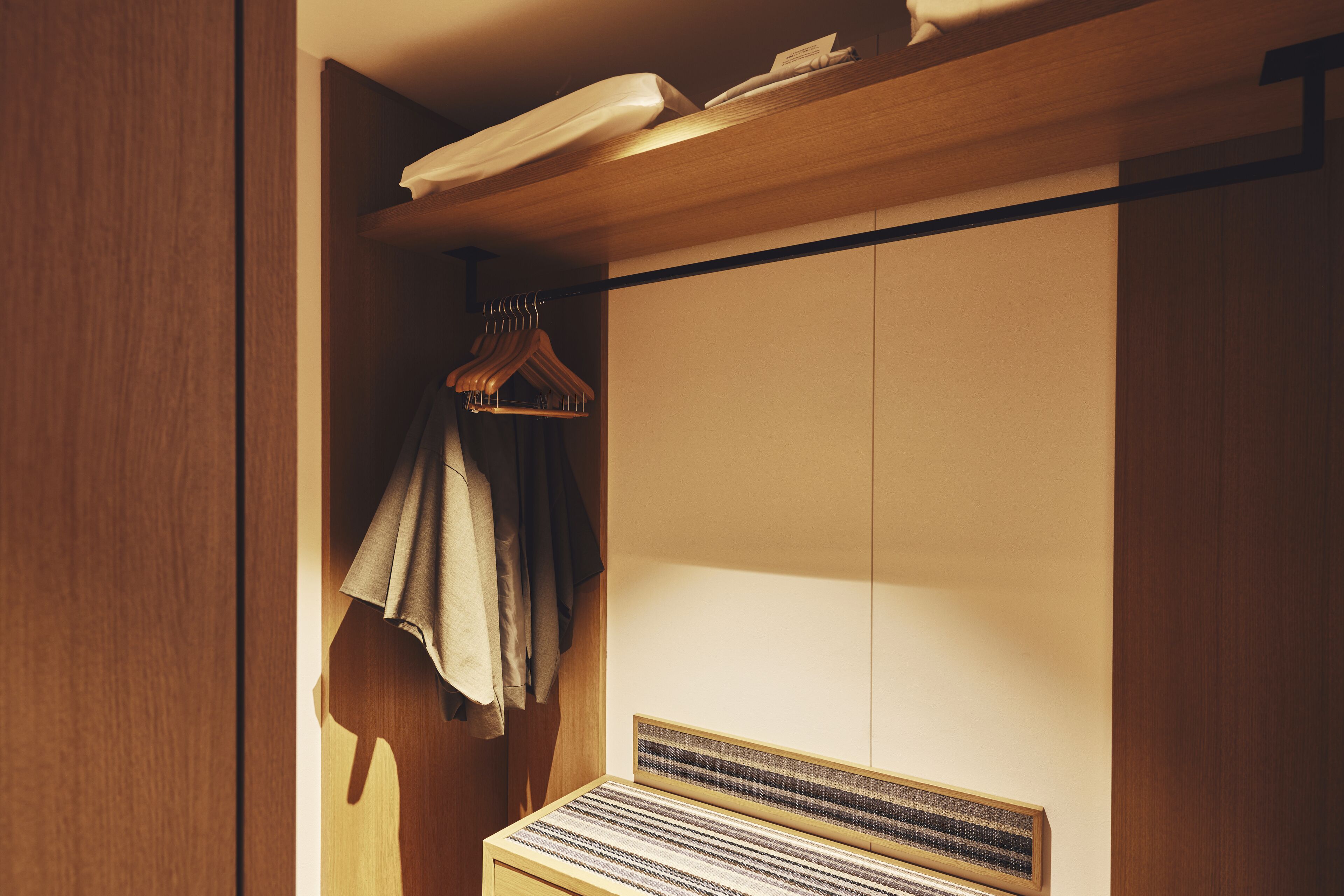 A wooden wardrobe with a hanging rack and a bed with a striped headboard.