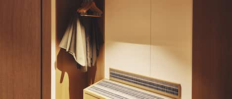 A wooden wardrobe with a hanging rack and a bed with a striped headboard.