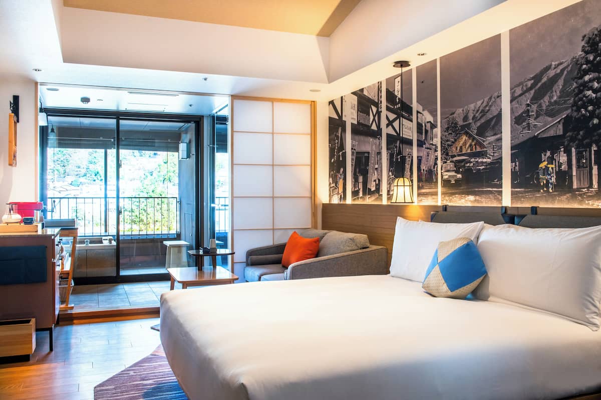 A modern hotel room with a large bed, a desk, and a seating area.