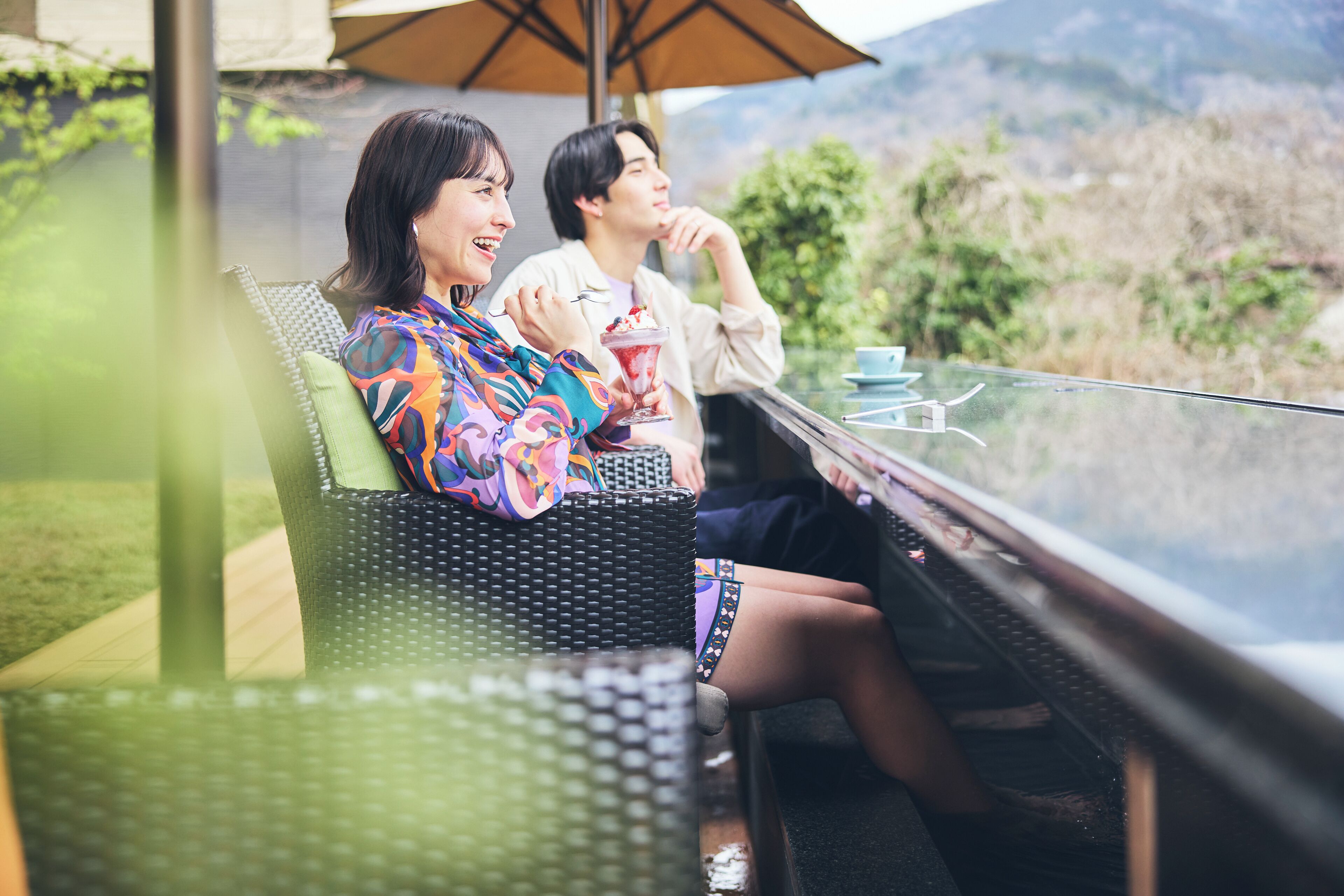 Two people sitting on wicker chairs at a glass table with a mountain view.