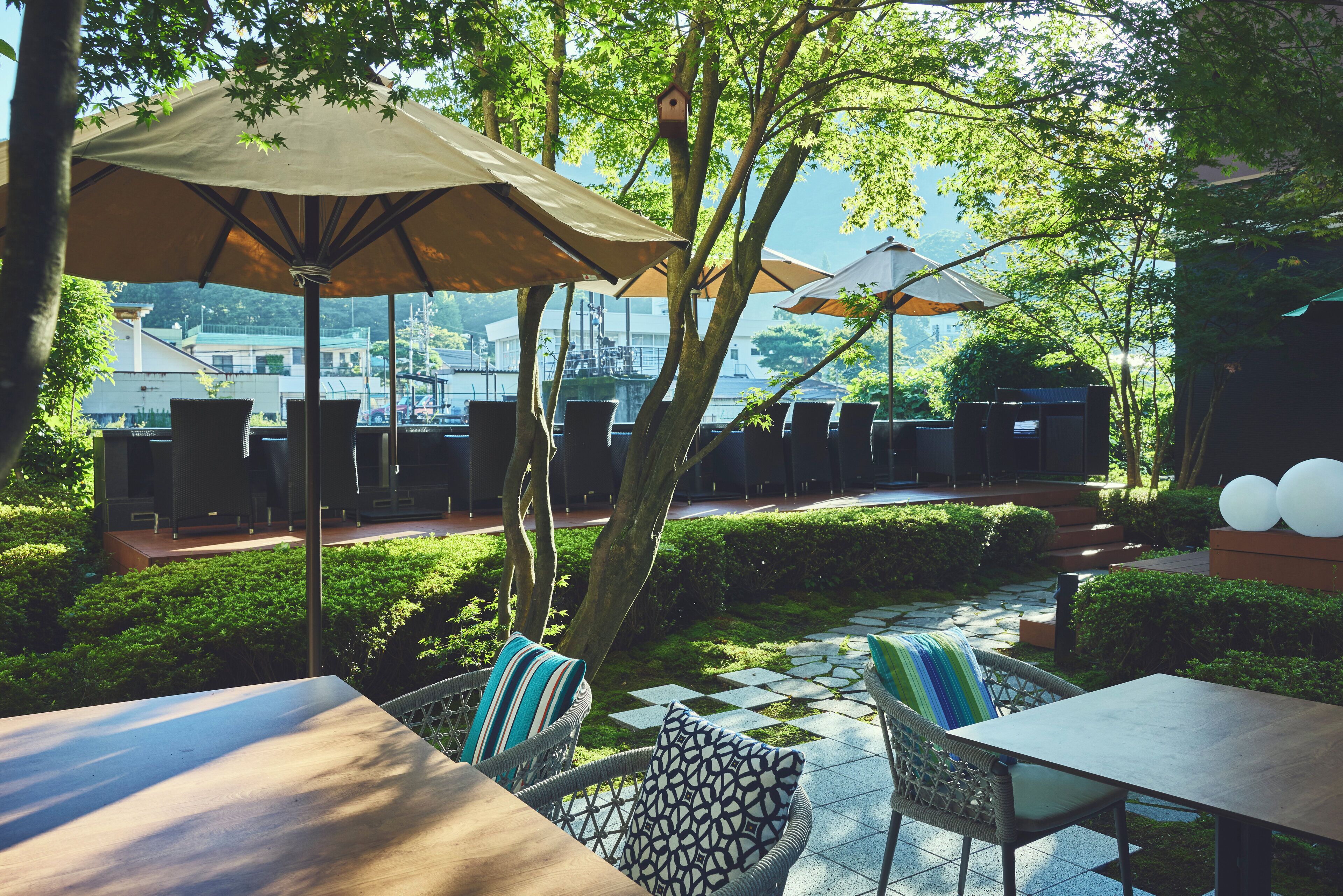 An outdoor patio with wicker furniture, large umbrellas, and a view of buildings in the background.