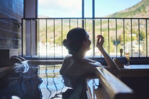 A person in a hot tub with a view of a mountainous landscape through a window. - Hotel Indigo Hakone Gora by IHG (Hakone)