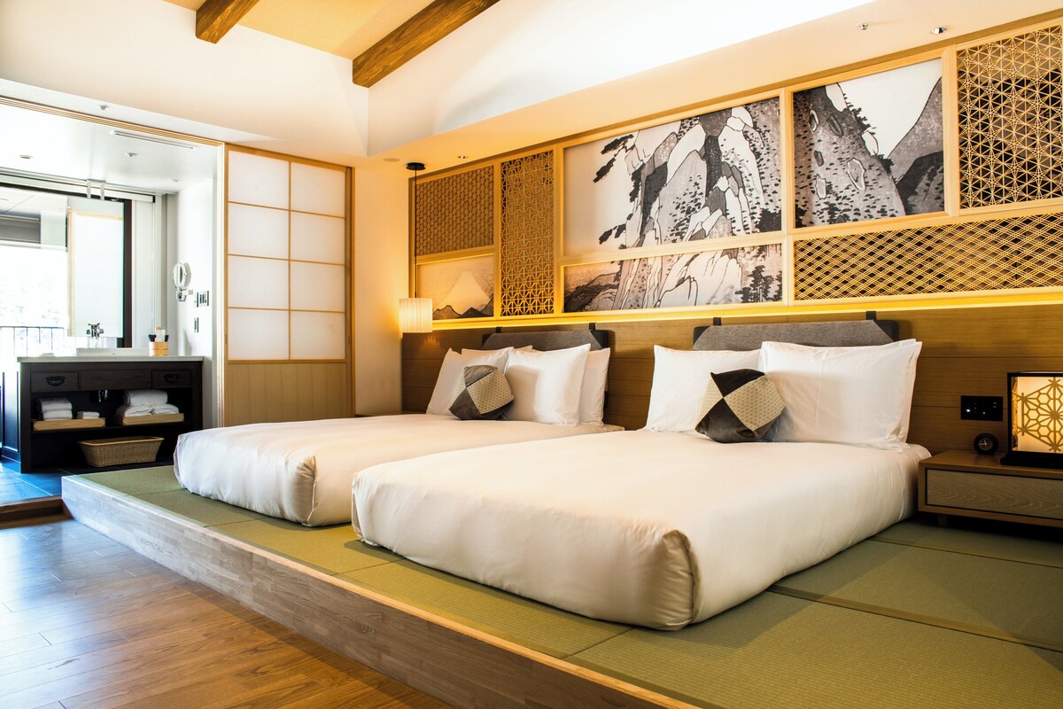 Habitación de hotel con dos camas, cabecera de madera, suelo de esteras de tatami y puerta corrediza tradicional japonesa.
