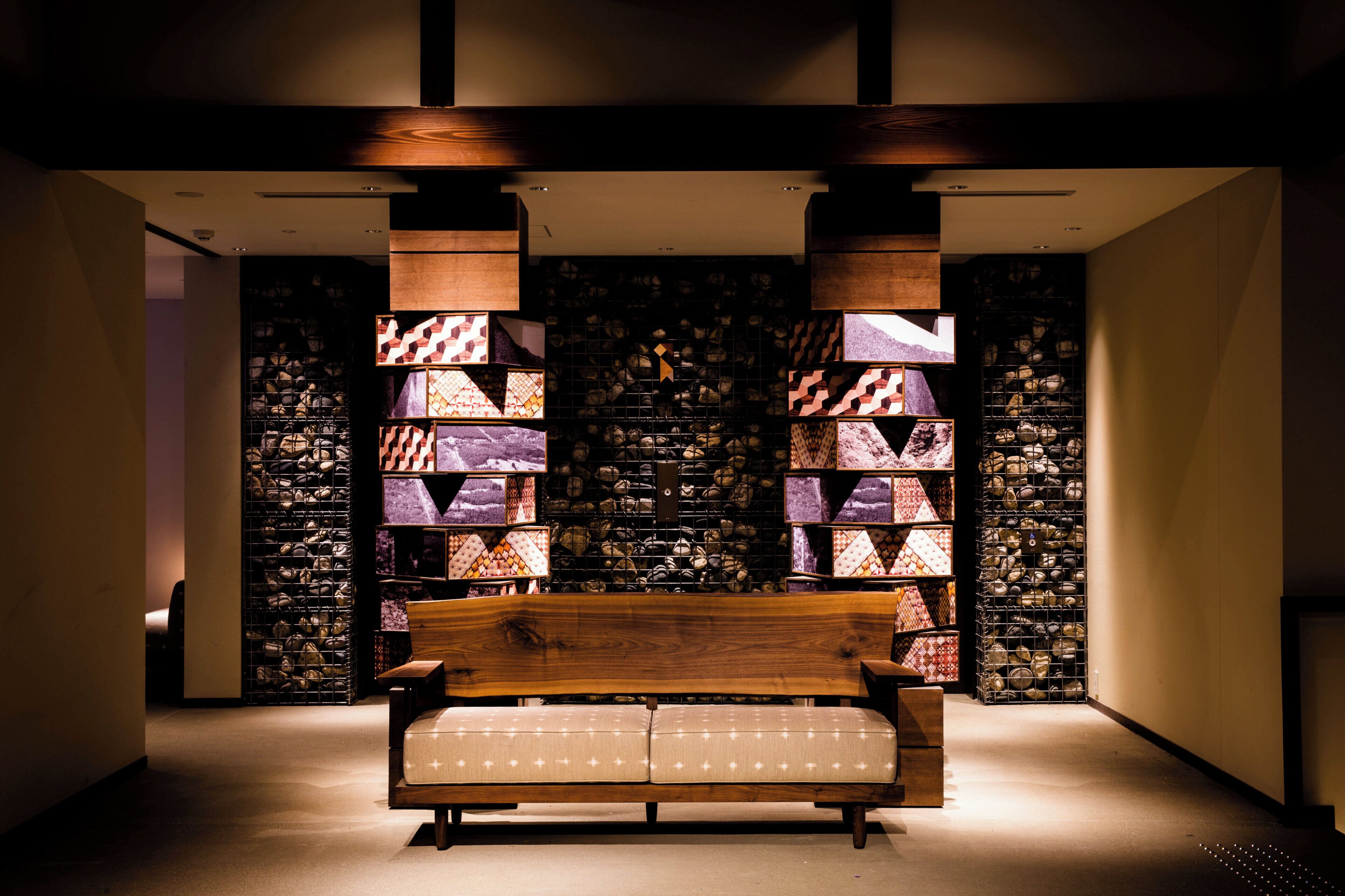 A modern interior with a wooden bench, a stone wall, and a series of framed patterns.