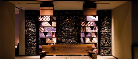A modern interior with a wooden bench, a stone wall, and a series of framed patterns.