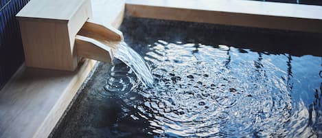 Una fuente de madera con un recipiente de madera y un flujo de agua que desemboca en una piscina reflectante.