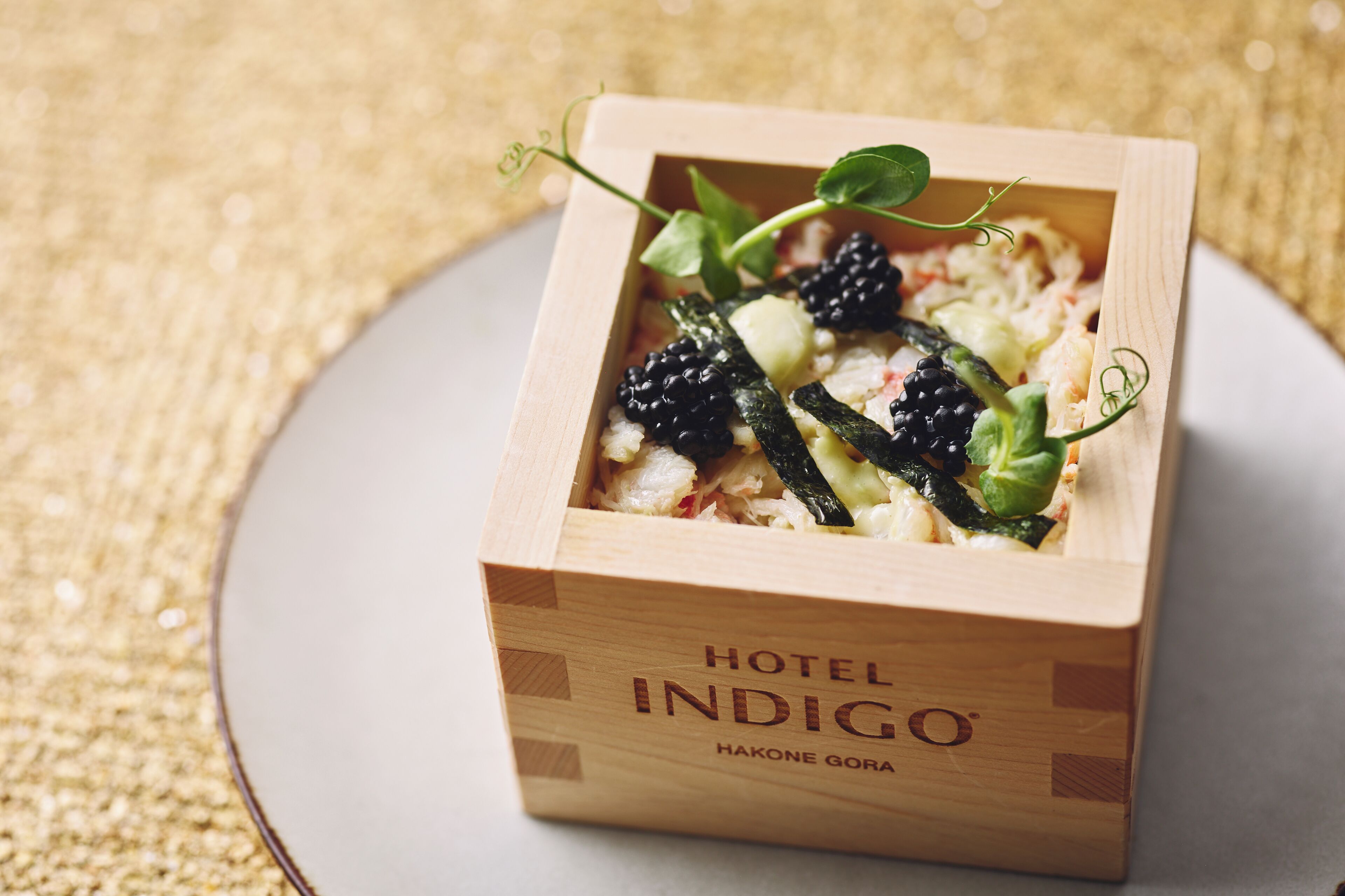 A wooden box labeled 'HOTEL INDIGO' with a dish inside, placed on a plate.