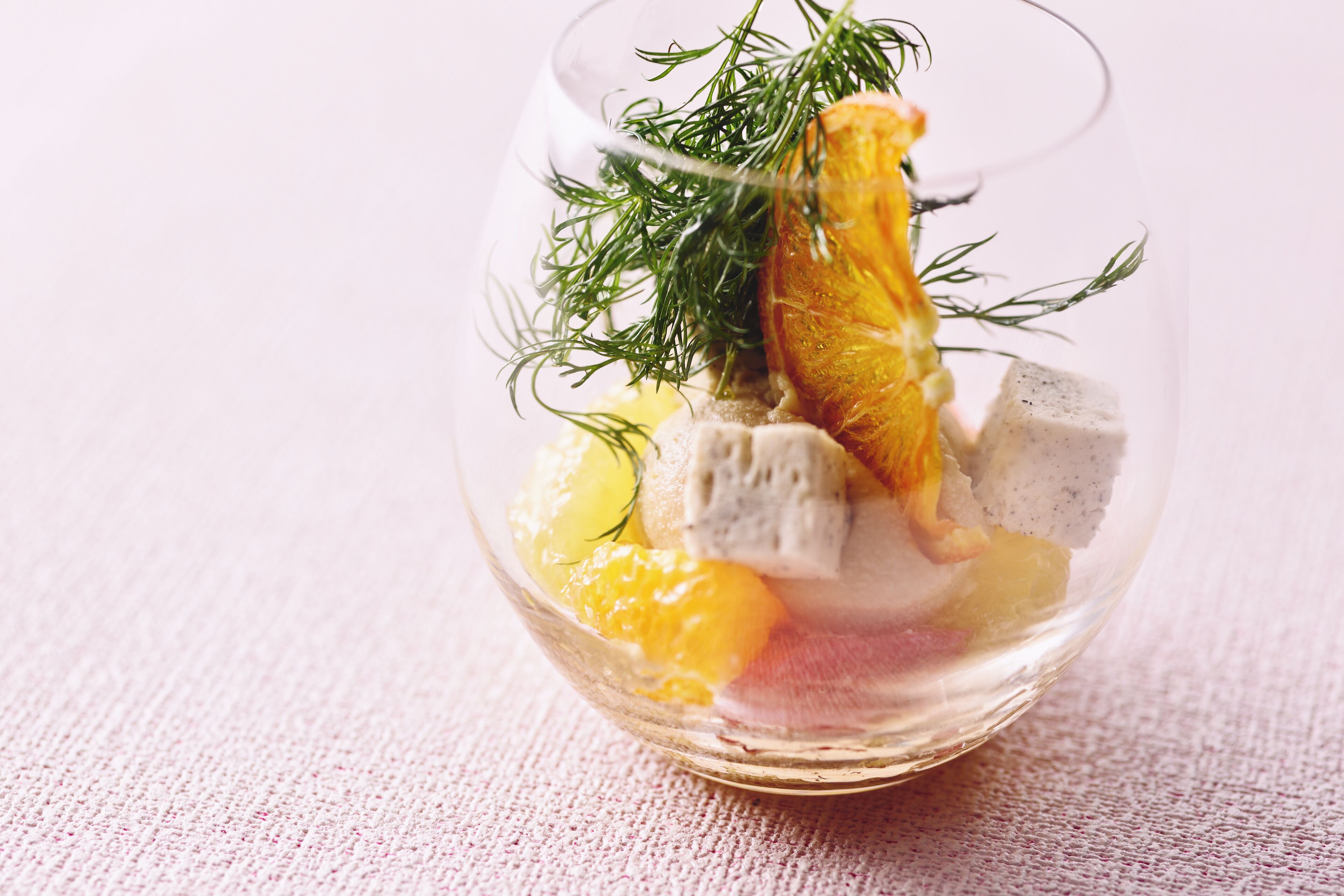 A clear glass bowl containing food items, possibly a salad or appetizer, with a piece of orange and green herbs.