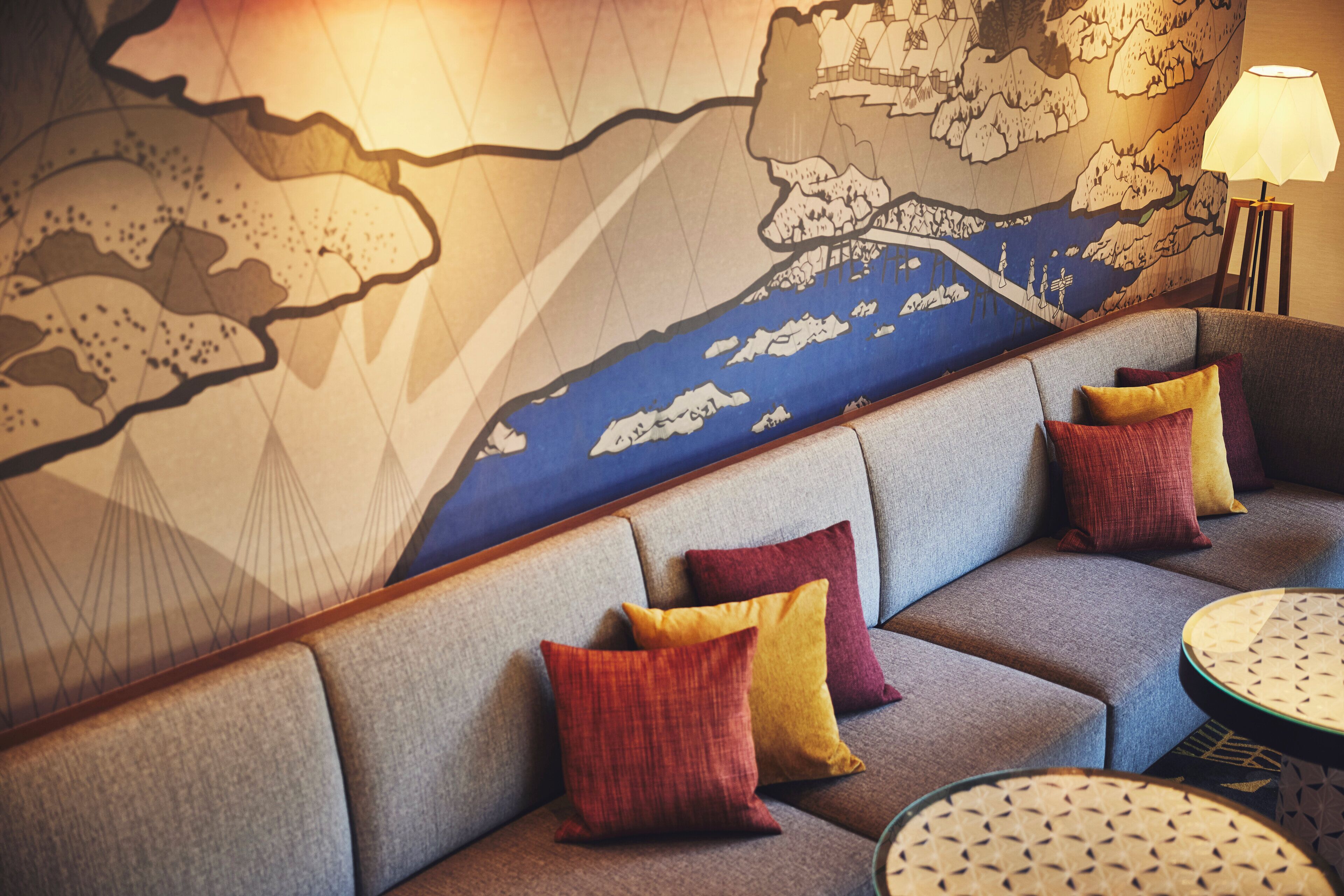A seating area with a sofa and round tables, a wall with a map design, and a lamp.
