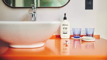 Un baño con un lavamanos blanco, una botella de loción corporal y dos vasos en la encimera.