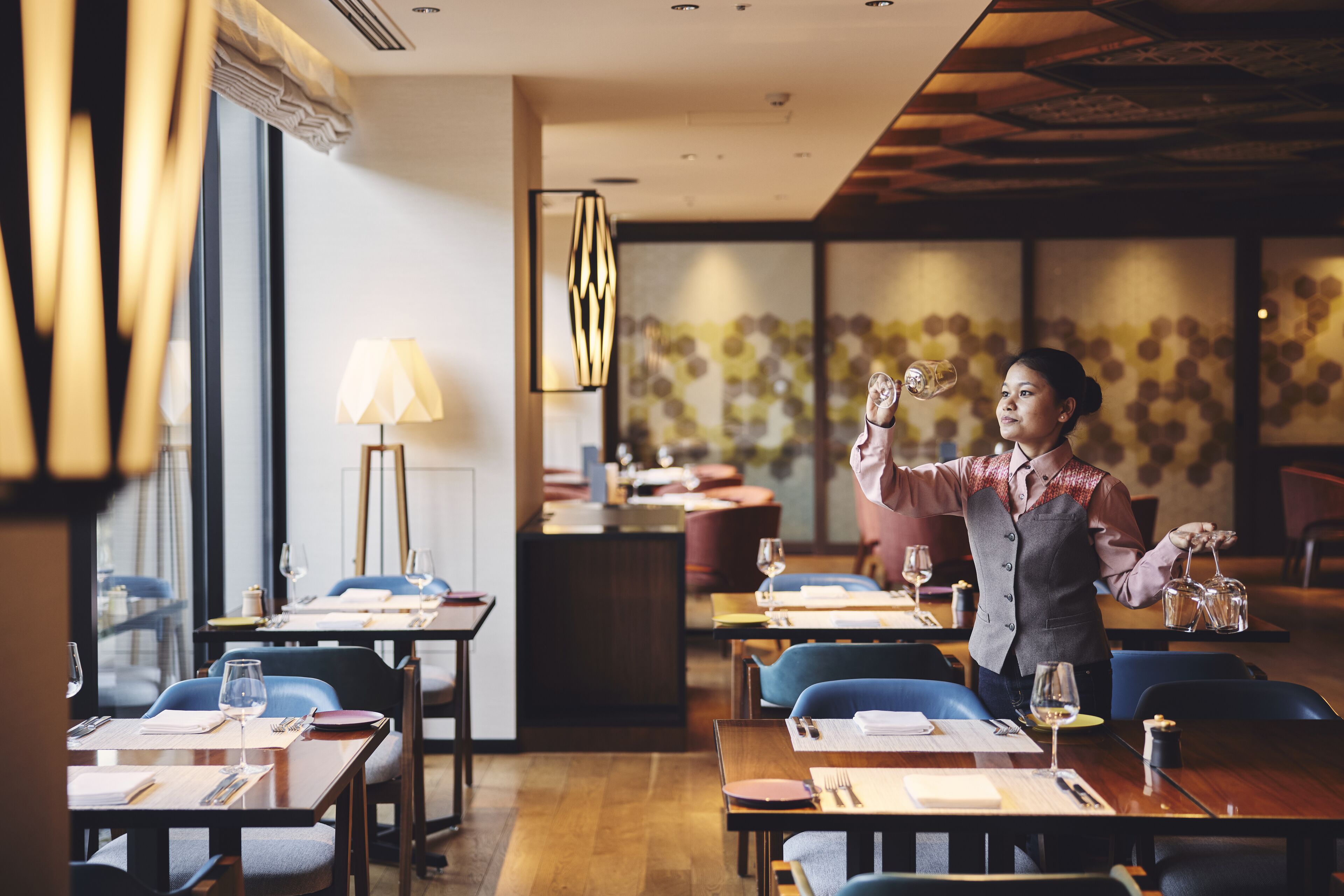 A restaurant with tables set for dining, a waiter serving a customer, and a modern interior design.