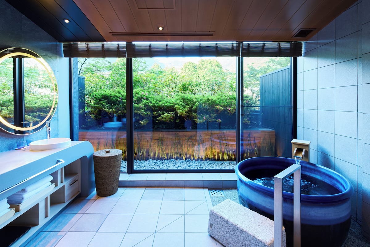 A modern bathroom with a large window, a round mirror, a sink, and a bathtub.