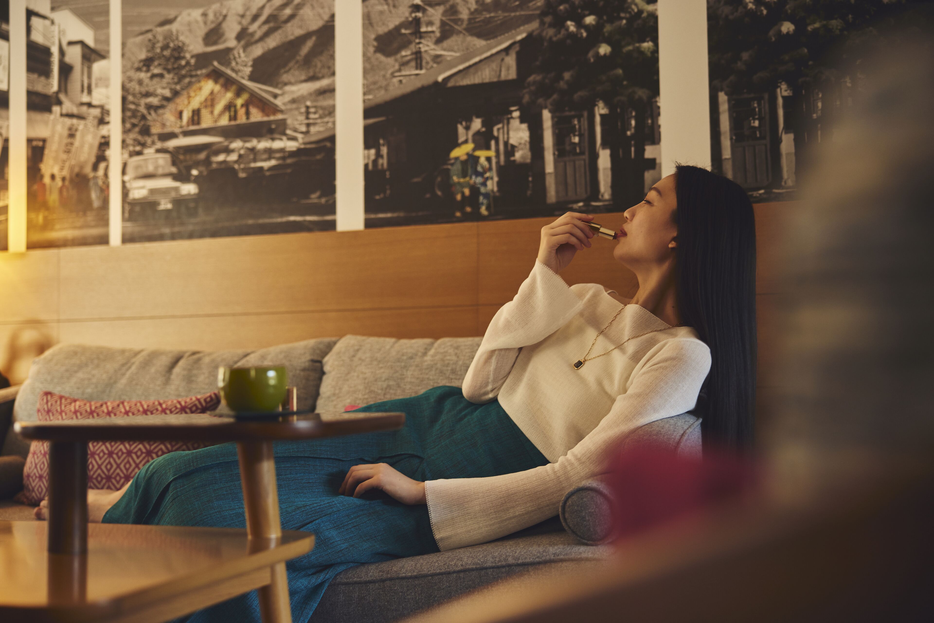 Una persona sentada en un sofá con una taza verde, una mesa de madera y una pared con fotografías en blanco y negro.